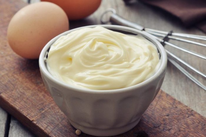 Homemade mayonnaise in bowl with eggs and spice on wooden background