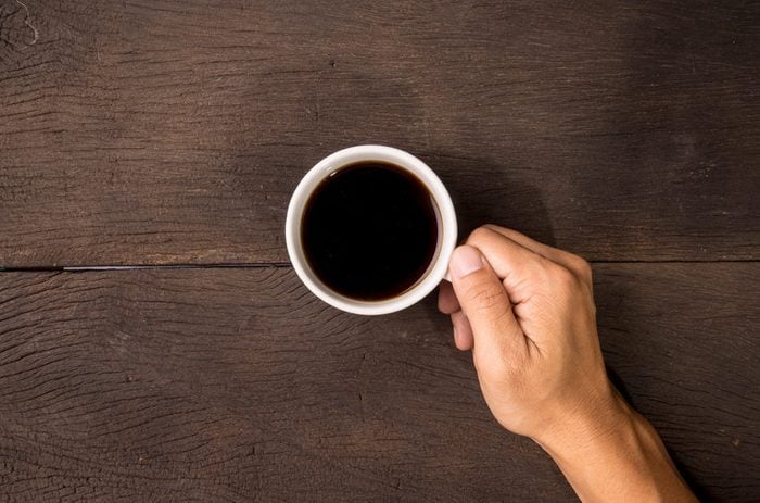 Male hand hold mug of espresso coffee on wood table.