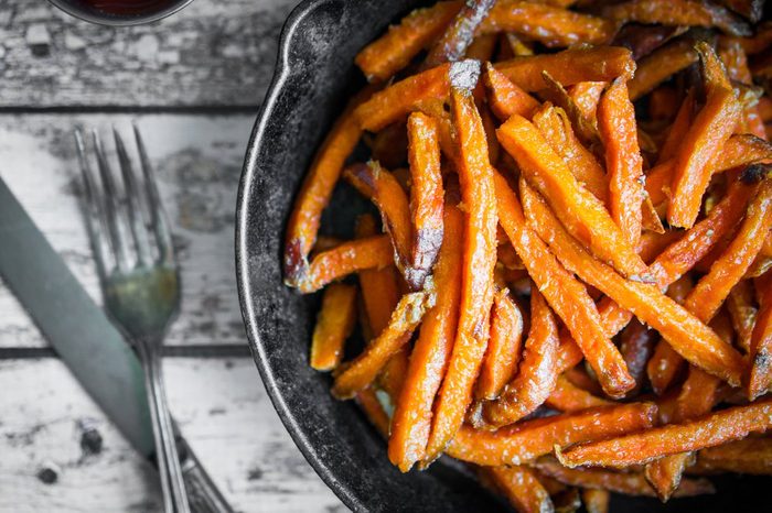 Sweet potato fries in cast iron skillet on wooden background