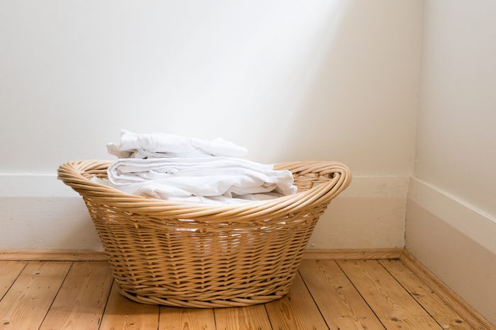 Wicker laundry basket with folded white washing on wooden floorboards with window light