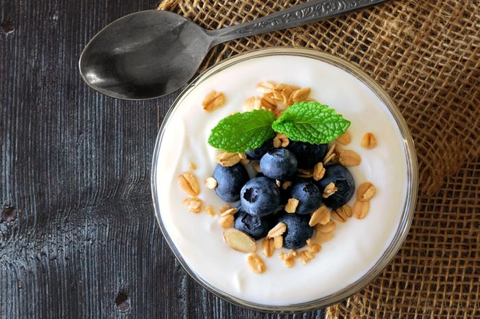 Yogurt with sweet blueberries and granola, above view on rustic dark wood