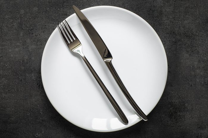 Table setting. Fork knife and white plate at dark slate table. Dark food background. Top view copy space.