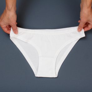 Women's hands holding white cotton panties on gray background. Woman underwear set. Top view.
