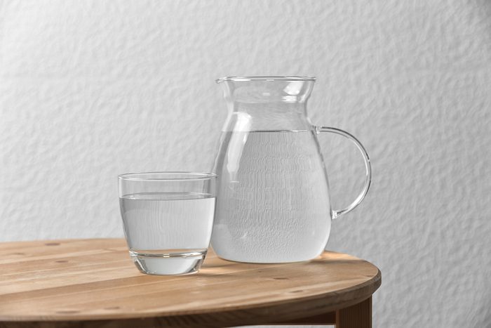 Pitcher and glass with water on table near white wall