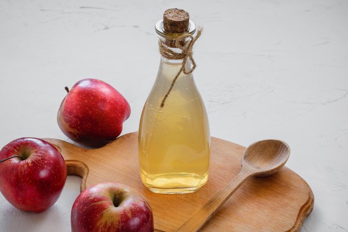 bottle of apple cider vinegar, spoon, and apples 