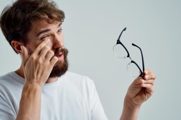 Bearded man rubbing his eye and holding his glasses.