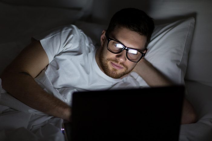 man in bed looking at his laptop at night in a dark room