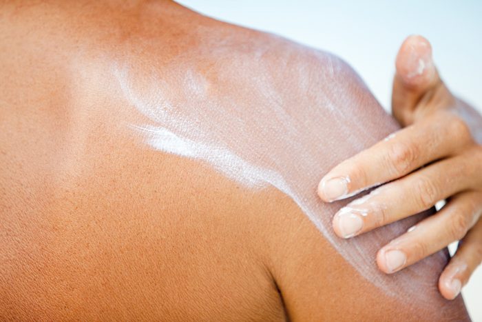 closeup of woman applying sunscreen to shoulder