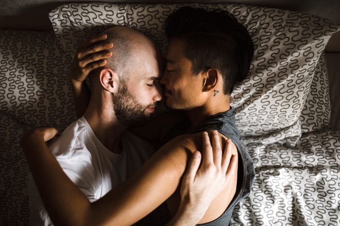 gay couple laying in bed together embracing
