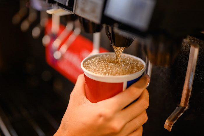 close up of person filling up cup at soda fountain