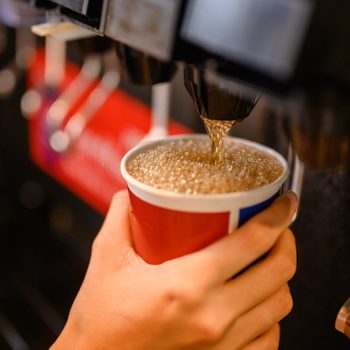 close up of person filling up cup at soda fountain