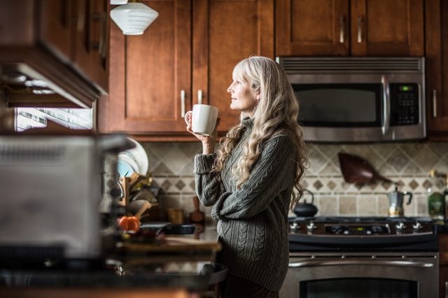 woman drinking morning cup of coffee in kitchen and looking out window