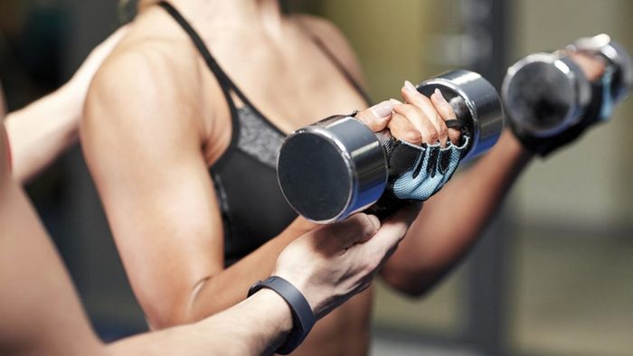 fitness, sport, bodybuilding and weightlifting concept - close up of young woman and personal trainer with dumbbells flexing muscles in gym