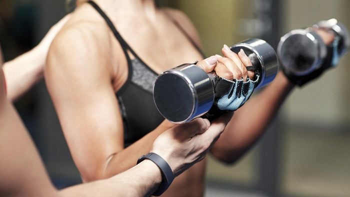 fitness, sport, bodybuilding and weightlifting concept - close up of young woman and personal trainer with dumbbells flexing muscles in gym