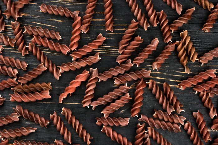 Background from scattered dark raw pasta fusilli on wooden background, top view