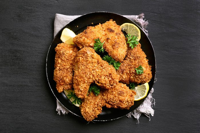 Fried breaded chicken wings on plate over black background