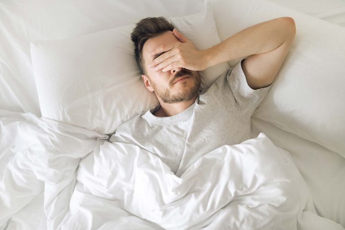 man in bed holding his hand over his eyes, exasperated