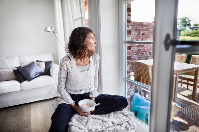 woman sitting at home eating lunch and looking out the window