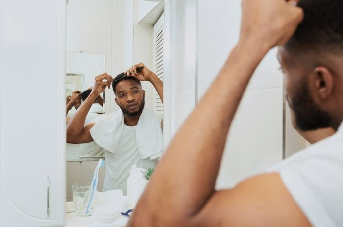 man examining hair in bathroom mirror