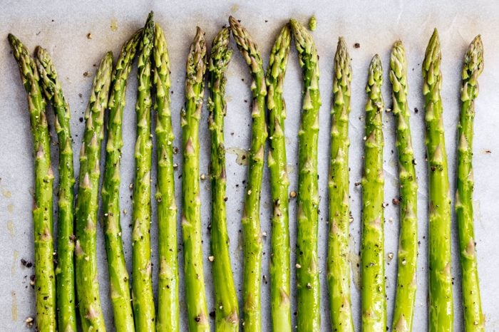 Asparagus spears on parchment paper over oven tray