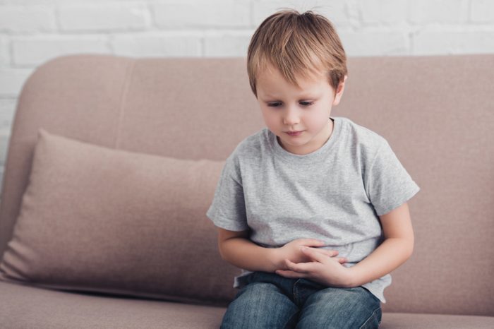 sick boy with stomach pain sitting on sofa in living room