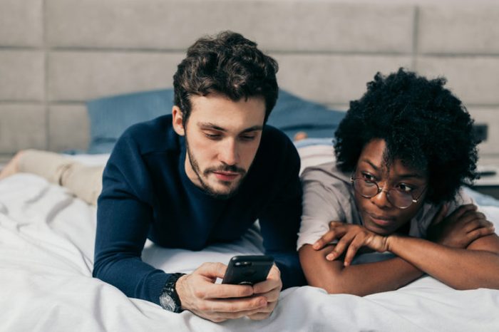 Internet social network addicted young married couple using their mobile phone in bed ignoring each other as strangers. Relationship and Communication problems concept