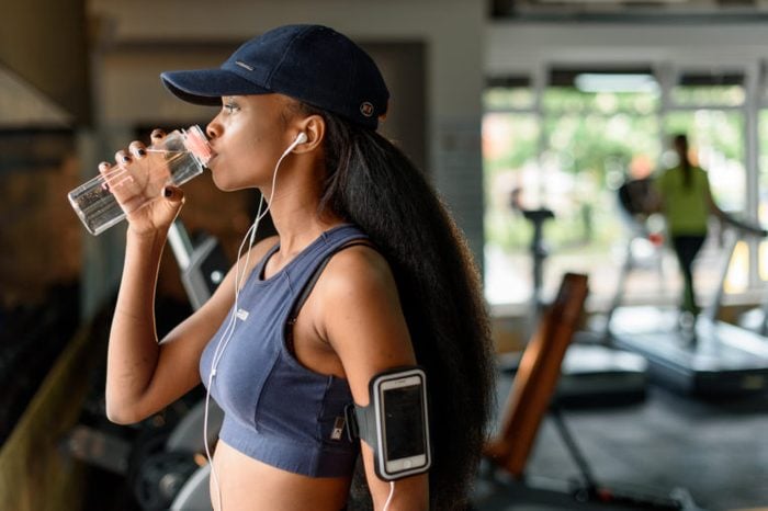 Side view of black female athlete drinking water from bottle in the gym