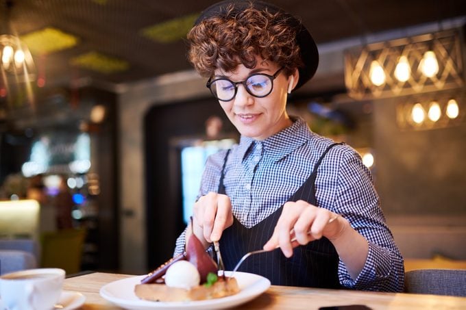 Young woman taking piece of pear dessert off her plate while sitting in cafe at lunch break