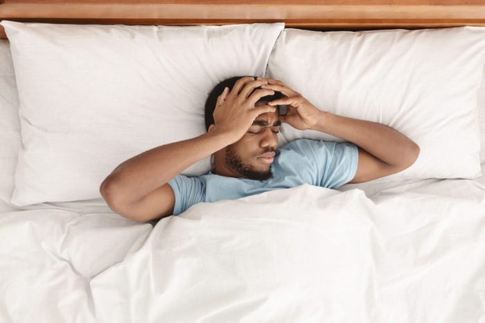 Restless african american man waking up with headache, lying in bed early in morning, top view