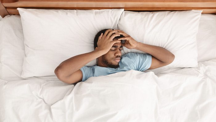Restless african american man waking up with headache, lying in bed early in morning, top view