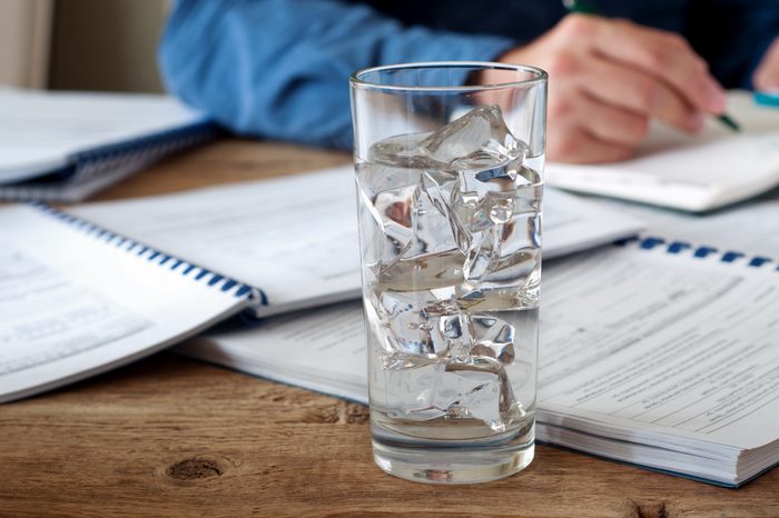 Glass of water with ice on a wooden office table. Against the background of a glass of water running man. Copy space