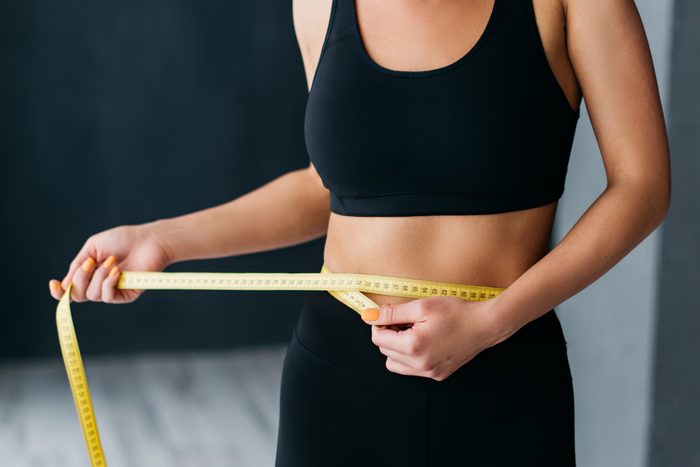 Woman in black sports bra and leggings measuring her waist 