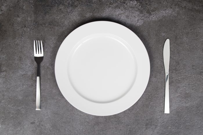 White empty plate with fork and knife on grey background