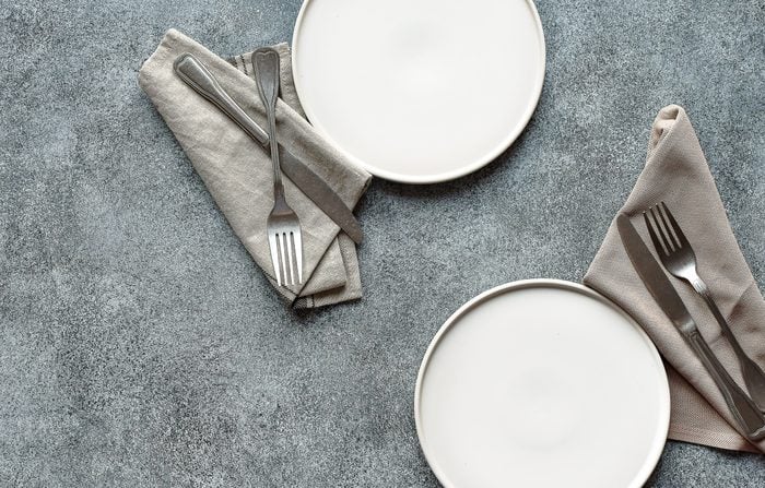 Two white plates, cloth napkins, and silverware on a slate background