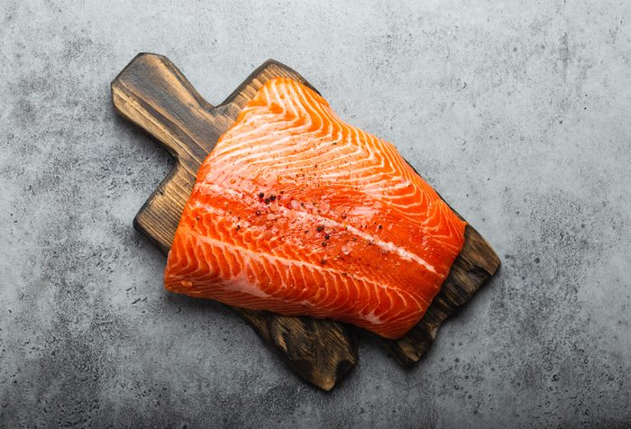 Top view, close-up of whole fresh raw salmon fillet with seasonings on wooden board, gray stone background. Preparing salmon fillet for cooking, healthy eating concept 
