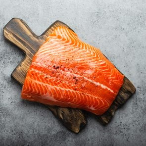 Top view, close-up of whole  fresh raw salmon fillet with seasonings on wooden board, gray stone background. Preparing salmon fillet for cooking, healthy eating concept 