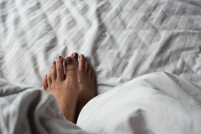 Close up of the feet of a young lady on the bed under white blanket. Foot tip beetle from blanket when lying in bed enjoying sensual foreplay. Holiday and relax concept.
