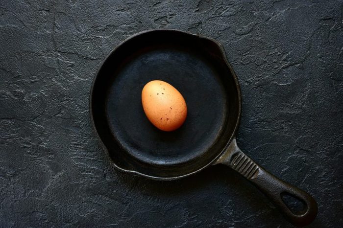 Fresh uncooked egg on a cast iron pan over black slate, stone or concrete background.Top view with copy space.