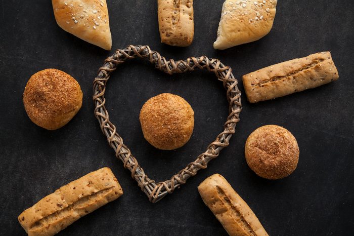 Concept of gluten free buns for allergic people with disease. Variation of bread with wooden heart shape on dark background.