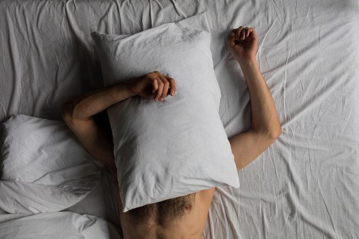 top view of shirtless man hiding face with pillow while sleeping in bed