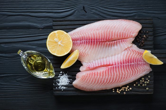 Fresh tilapia fillet ready to be cooked, black wooden background, top view