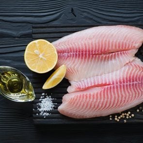Fresh tilapia fillet ready to be cooked, black wooden background, top view