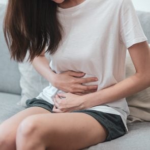 Healthcare medical or daily life concept : Close up stomach of young lady have a stomachache or menstruation pain sitting on a sofa.