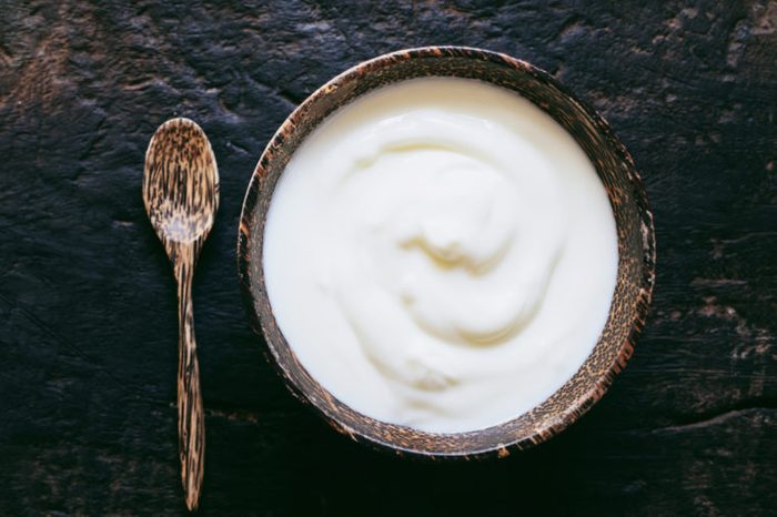 Greek yogurt or sour cream in a wooden bowl on dark table top view. Healthy food nutrition.