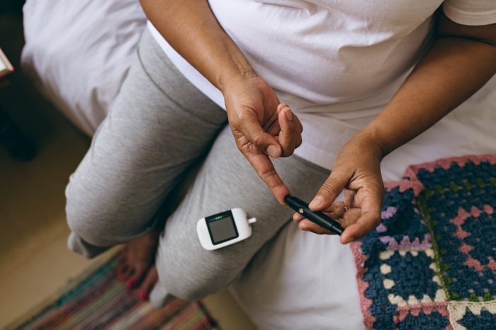 Low section of mixed race female senior patient checking blood sugar level with glucometer at retirement home 