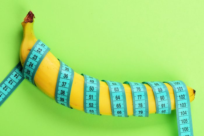 Banana with blue tape for measuring figure. Centimeter ruler spinned around fruit. Blue tape wrapped around banana isolated on light green background. Weight loss, healthy food and slim body concept.