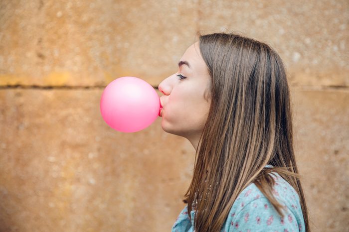 teen girl blowing a pink bubble with bubble gum