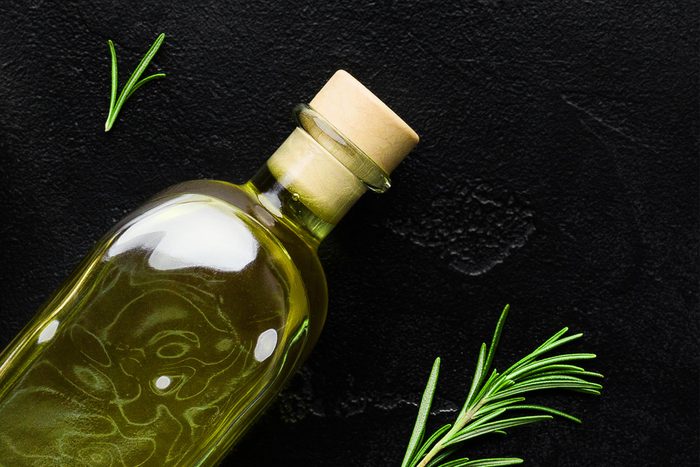 Olive oil in bottle , fresh olives and rosemary sprigs on black background, top view. Organic olive oil concept