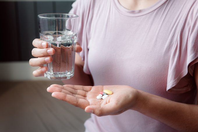 cropped shot of woman holding supplements and glass of water