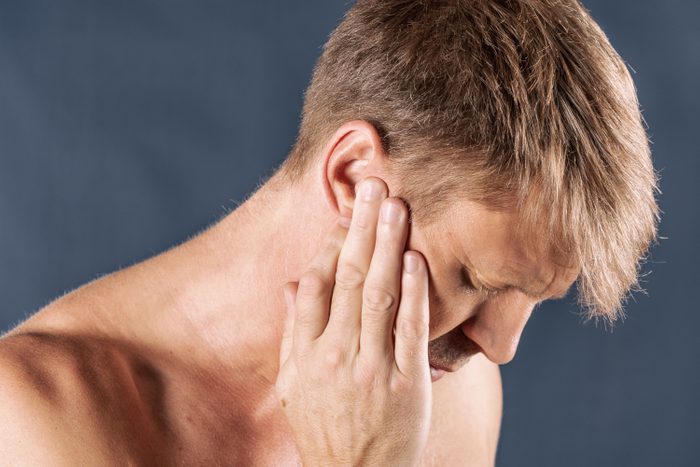 Man has a sore ear. Man suffering from headache on blue background